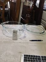 Full view of the Pyrex glass roaster and lid displayed on a white cloth with a pen for scale and a lot tag showing item number 937.