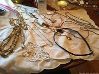Image showing a collection of assorted goldtone and silvertone necklaces, some with rhinestones, arranged on a white cloth.