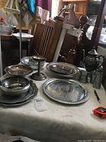 Photo showing variety of metal items on table including trays, chalice, cups, and containers.