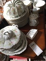 Photo showing stacked china pieces including plates, cups, and serving dishes with floral designs and gold accents.