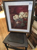 Photo showing a framed painting of white hydrangeas, double matted and under glass. The frame is ornate with a gold finish. The painting is positioned on a wooden floor surface.