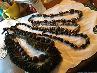 Four large chunky necklaces laid out on a white cloth surface showing color tones of black, gold, and green with varied bead styles.
