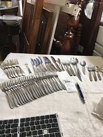 Image showing a collection of assorted flatware including forks, knives, spoons, and serving utensils spread in rows on a table.