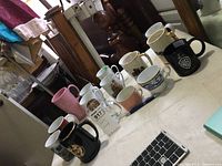 Photo showing 13 mugs of varying sizes and designs arranged on a table.