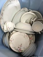 View of various plates, bowls, teacups, and saucers stacked in a bin, showing floral china pieces.