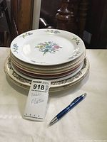 Stack of 7 assorted decorative plates showing floral patterns and borders in various colors, lightly used condition