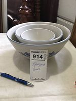 Set of three nested Pfaltzgraff bowls showing blue floral pattern and cream background color with a pen and lot tag for scale.