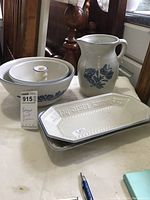 Photo showing all items in the lot: two matching bowls stacked, one pitcher, two bread platters stacked. The items have a white base color with blue floral decoration and blue-rimmed edges.