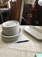 Stacked white ceramic luncheon and bread & butter plates with blue floral pattern and blue rim, arranged on table to show quantity and design.