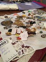 Top view of assorted pins, pendants, sweater clips, buttons, and shoe clips laid out on a white cloth with lace trim.