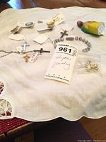 Photo showing multiple religious-themed jewelry pieces including crosses, pins, bracelet, and a small figurine on a white cloth.