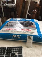 Photo of snow chains in original packaging with SCC Security Chain Co. branding and easy mounting instructions on a table with various household items nearby.