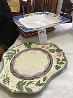 View showing 4 stacked square platters with colorful rims and 1 uniquely shaped non-square platter with strawberry design on green rim.