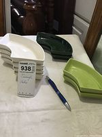 Nine triangle shaped ceramic dishes stacked by color on a table: five white, two dark green, two light green. Pen for size reference.