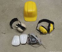 Full lot overview showing yellow Welsh Co bump hat, two sets of ear protection earmuffs (black/white and yellow/black), 3M half mask respirator, and two replaceable white cartridge filters.