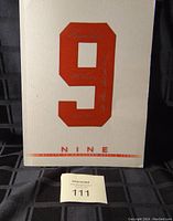 Front cover of the autographed book showing the large red number 9 with signatures.