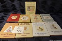 Ten small hardcover Beatrix Potter books arranged with front covers visible, including multiple classic titles with illustrated animal characters. Shelf background.