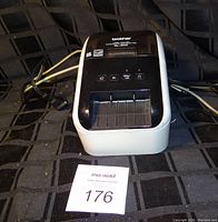 Front view of the Brother QL-800 label printer showing the main unit with power cord laid behind it and the MaxSold auction tag in front.