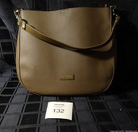 Front view of brown textured purse with gold-tone brand plaque and attached shoulder strap