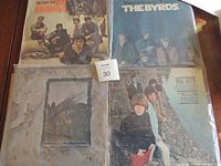 Four vintage vinyl LP records with original cover artwork laid out on a wooden table showing The Animals, The Byrds, Led Zeppelin, and The Rolling Stones albums.