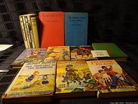 Top view of 14 vintage hardcover books arranged in two rows, showing front covers and partial titles.