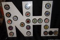 NHL-shaped white display case holding 21 different NHL team hockey pucks arranged inside clear circular compartments.