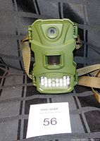 Closed unit showing front lens, motion sensor, and infrared LED array on green plastic case with attached strap for mounting.