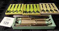 Overview of three spoon sets in original packaging along with a 4-piece silver plated cutting tool set in a green box.