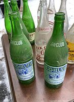 Photo showing front row of green Ski Club bottles and clear Elk Club bottles in back, all vintage soda bottles