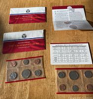 Photo of two 1987 US Uncirculated Coin Sets in original envelopes with two informational sheets laid flat on wood surface. Each coin set has seven coins in sealed clear plastic holders.