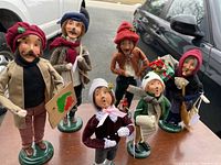 Wide shot showing all six Byers Choice caroler figurines arranged on table outdoors, sunlight exposure highlights fine details and colors