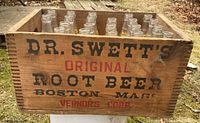Front view of wooden crate with stamped labeling 'Dr. Swett's Original Root Beer Boston Mass Vernor's Corp' showing 21 glass bottles inside.