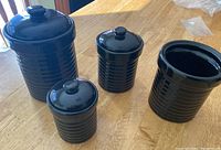 Four dark blue ceramic kitchen canisters on wooden table, three have lids and one does not.