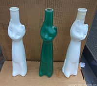 Three cat face bottles displayed side by side: two white and one aqua green with visible scratch on one white bottle.