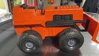 Side view of bright orange Mighty Mo bulldozer toy with four large black tread wheels and detailed rear section.