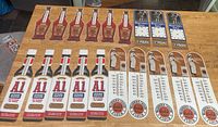 Full lot display of all thermometer advertising inserts showing A1 steak sauce bottles, Heinz ketchup bottles, Washburn Crosby Gold Medal Flour flower thermometers, and insult clock inserts arranged in rows on table.