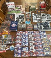Wide view of table showing all items including unopened baseball flipbooks, vintage photos, card sets, mugs, lunchbox, and assorted memorabilia.