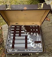 Open leather suitcase showing organized combination wrenches held by brown leather straps