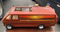 Side view of the red vintage Tonka safari van with sunset landscape decals and driver figure behind it.