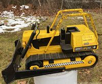 Side view of vintage Tonka Turbo-Diesel bulldozer showing yellow metal body, black plastic blade, and rubber tracks on grassy outdoor surface.