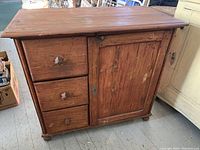 Front view of antique wooden cabinet with three drawers on left and single door on right, showing overall finish and handles.