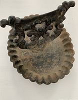 Top view of antique cast iron boot scrape showing decorative handle and scalloped tray with dirt and wear consistent with outdoor use.