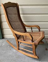 Side angle showing antique child's rocking chair with curved armrests and caned seat and back