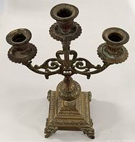 Top-down view of three-arm brass candelabra with ornate candle holders and engraved details on arms and base.