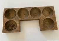 Top view of antique wooden cash drawer insert showing six round recessed compartments and a cut-out section along the bottom edge.