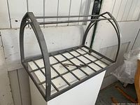 Overall view of metal hanging pot rack showing grid base and curved side supports.