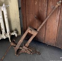 Side view of large antique iron vise rusted with long handle against wooden wall and radiator.