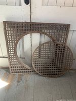 Square cast iron grate frame and circular grate insert leaning against wall