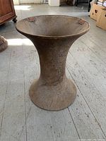 Large industrial cast iron fitting with a flared hourglass shape, rusty and worn, standing on a wooden floor indoors with daylight lighting.