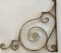Close-up view of the large central spiral and smaller scrolls in the iron hook, showing the white paint with vintage wear and rust.